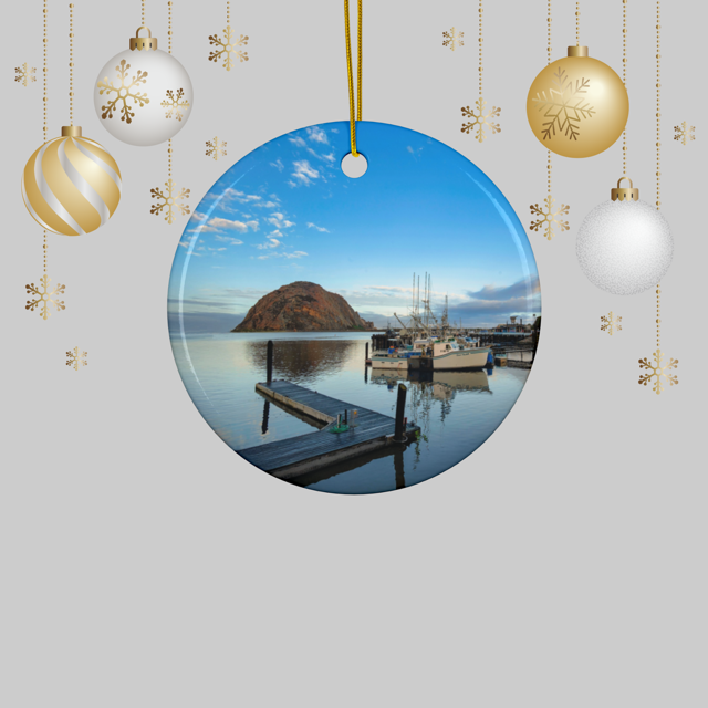 Ceramic Christmas ornament featuring an early morning photograph of Morro Bay harbor with boats, a pier, and Morro Rock reflected in the calm water, hanging against a light gray background.