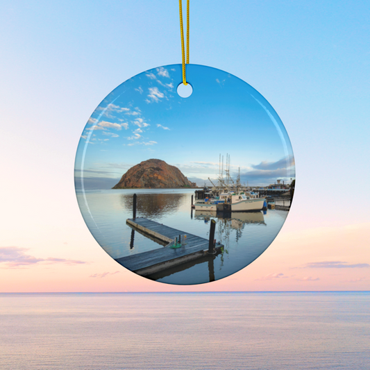 Ceramic Christmas ornament featuring an early morning photograph of Morro Bay harbor with boats, a pier, and Morro Rock reflected in the calm water