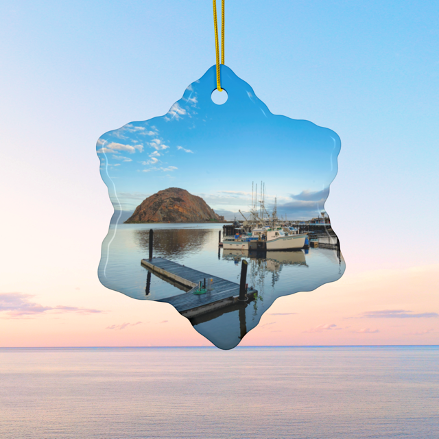 Ceramic Christmas ornament featuring an early morning photograph of Morro Bay harbor with boats, a pier, and Morro Rock reflected in the calm water, hanging against a blue sky.