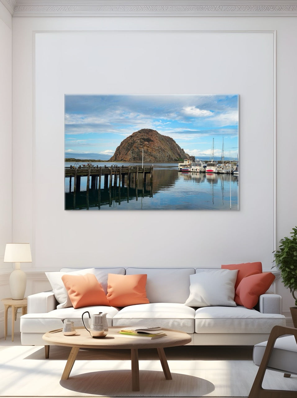 Living room with a large canvas print featuring a view of Morro Rock from the harbor in Morro Bay, California with boats and a pier, white sofa with colorful cushions, and wooden coffee table.