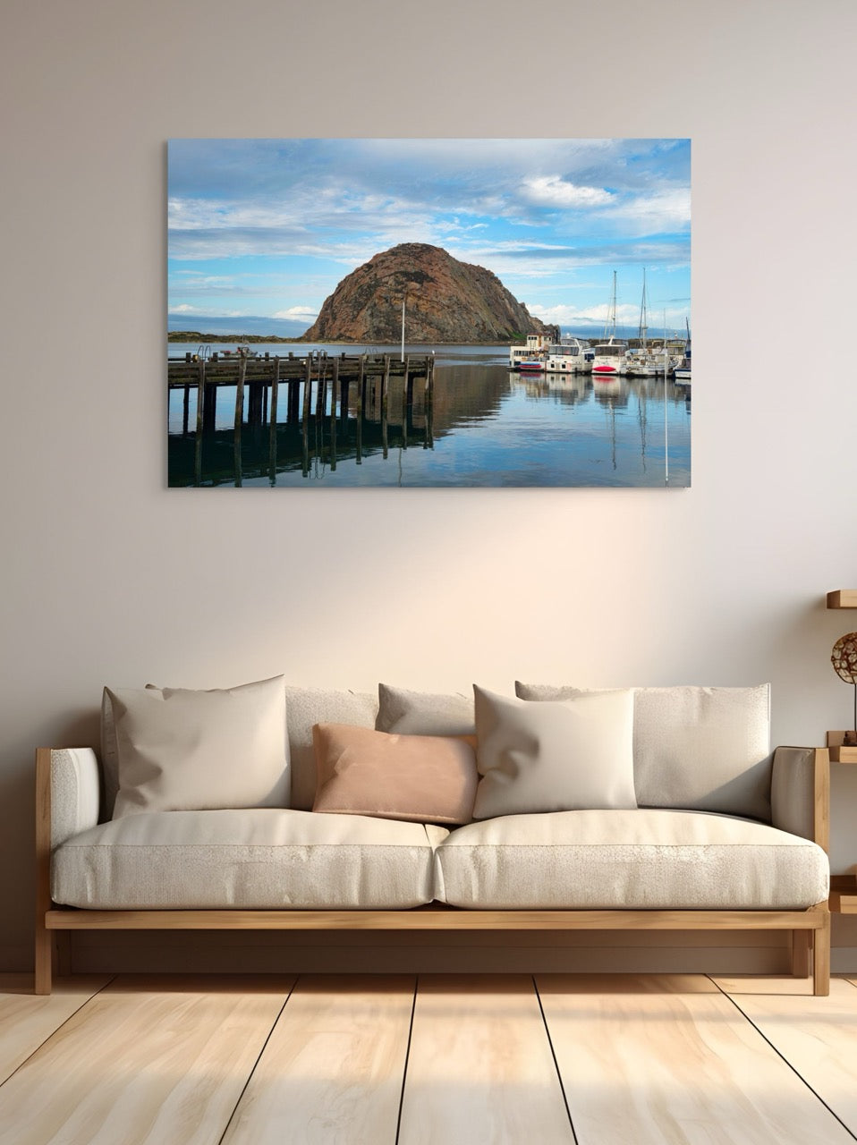 A large canvas print featuring a view of Morro Rock from the harbor in Morro Bay, California with boats and a pier. hanging above a sofa.