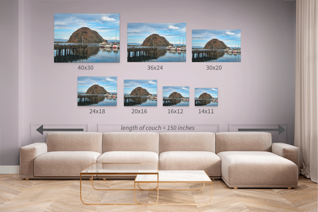 Wall art prints featuring a view of Morro Rock from the harbor in Morro Bay, California with boats and a pier with corresponding dimensions displayed above a beige sofa.