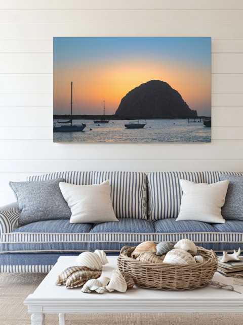Cozy living room with a striped sofa, decorative pillows, and a woven basket on a coffee table, featuring a large wall art of a Morro Rock sunset.