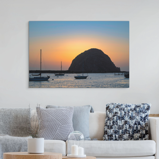 Canvas print of a Morro Rock sunset with boats, hanging above a living room sofa.