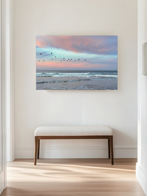 Canvas print of birds flying over pastel pink sunrise in Morro Bay on a wall above a wooden bench