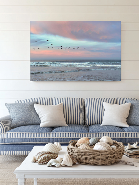 Living room with a couch, coffee table, and a large canvas print of birds flying over pastel pink sunrise in Morro Bay  on the wall.