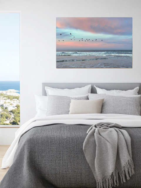 Bedroom with a canvas print of birds flying over pastel pink sunrise in Morro Bay.