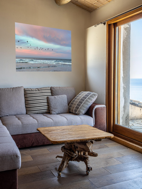 Living room with a gray sofa, wooden coffee table, and a large canvas print of birds flying over pastel pink sunrise in Morro Bay .