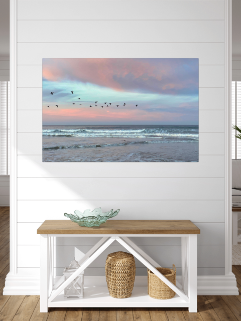 Canvas print of birds flying over pastel pink sunrise in Morro Bay on a wall above a wooden bench with storage.
