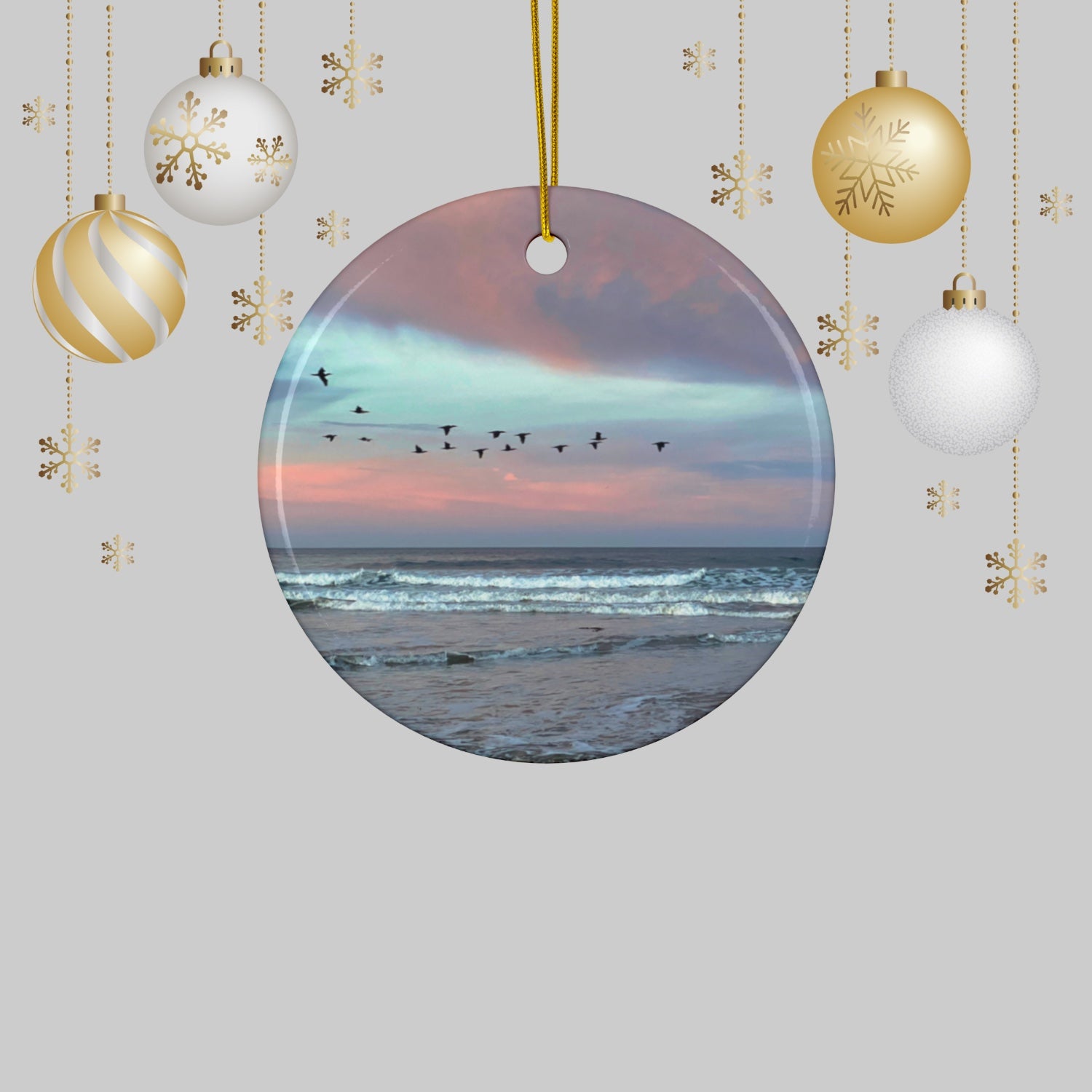 Ceramic holiday ornament featuring a photograph of a flock of birds flying across a pastel pink and violet sunrise sky over the Pacific ocean and Christmas ornaments on a light gray background