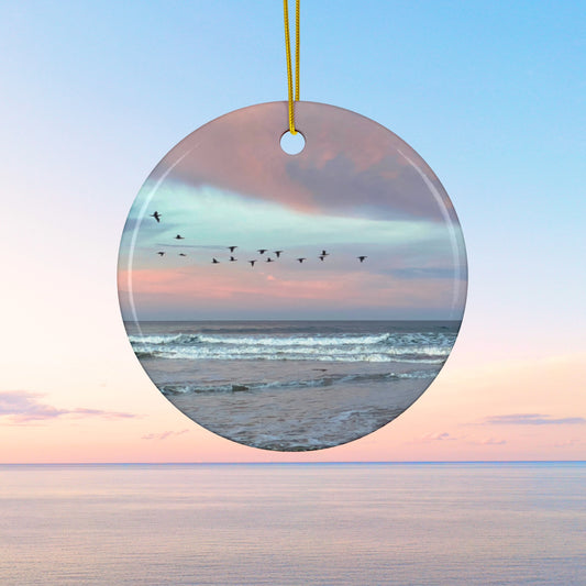 Ceramic holiday ornament featuring a photograph of a flock of birds flying across a pastel pink and violet sunrise sky over the Pacific ocean.