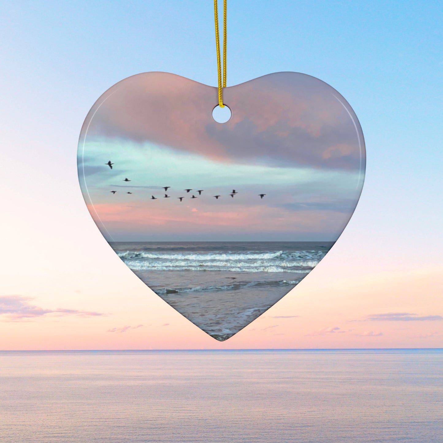 Heart-shaped ceramic holiday ornament featuring a photograph of a flock of birds flying across a pastel pink and violet sunrise sky over the Pacific ocean.