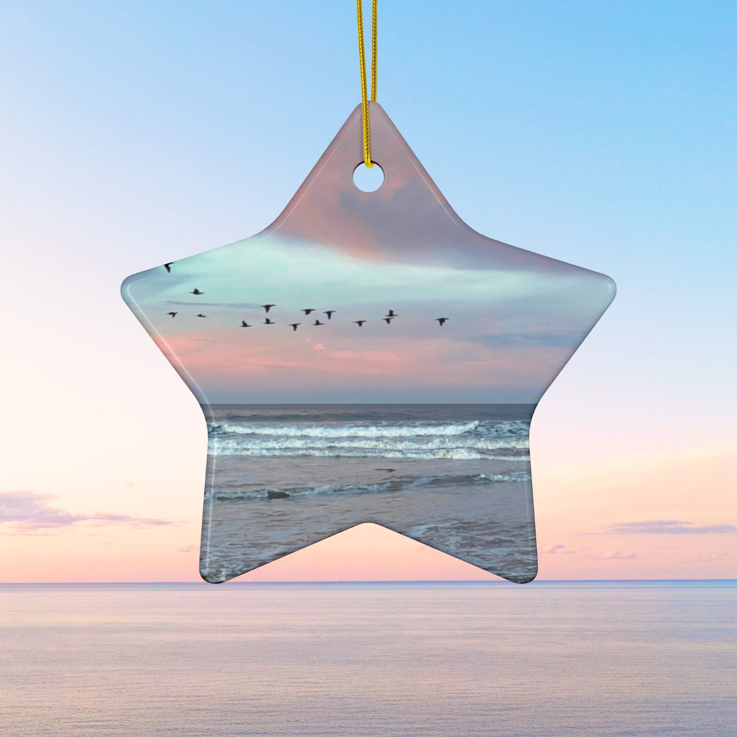 Star-shaped ceramic holiday ornament featuring a photograph of a flock of birds flying across a pastel pink and violet sunrise sky over the Pacific ocean.