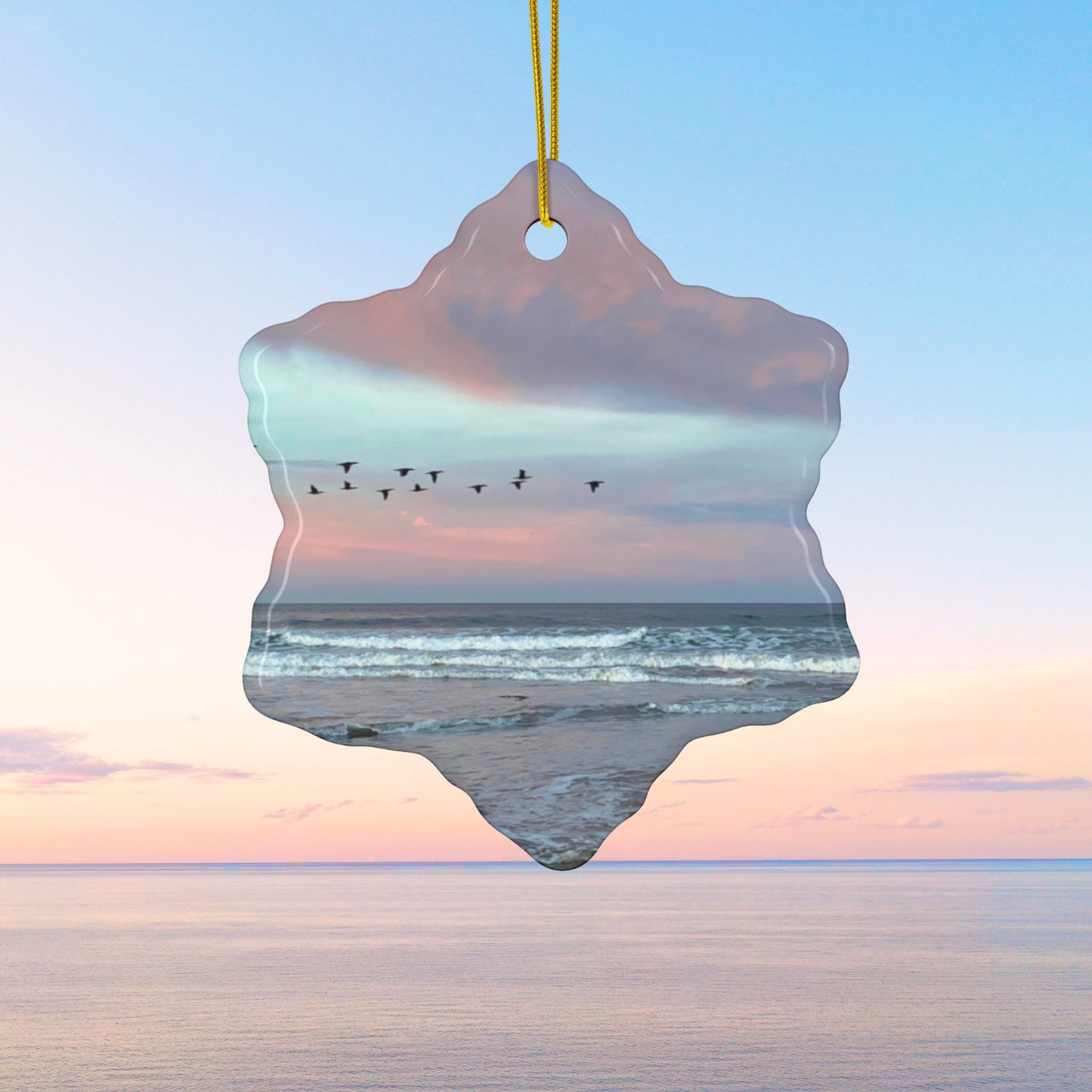 Ceramic holiday ornament featuring a photograph of a flock of birds flying across a pastel pink and violet sunrise sky over the Pacific ocean.