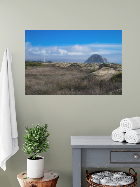 Morro Rock and stacks view from the beach dunes canvas print on a wall above a table with a plant and folded towels.