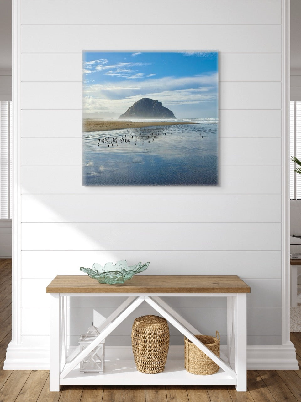 Canvas print of Morro Rock on a wall above a wooden bench with a glass bowl and baskets.