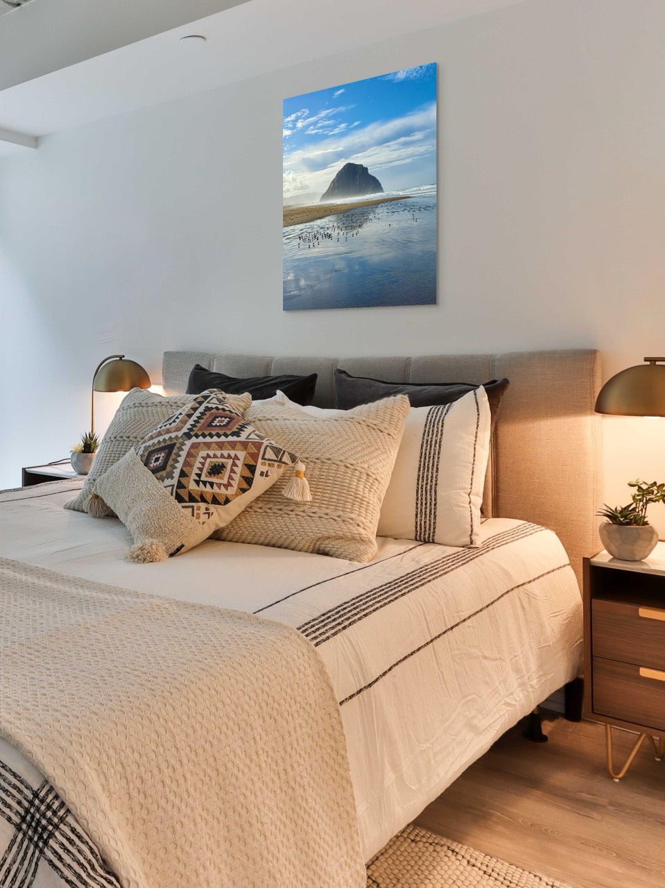Neatly made bed with decorative pillows in a bedroom setting, featuring a large canvas print of Morro Rock.