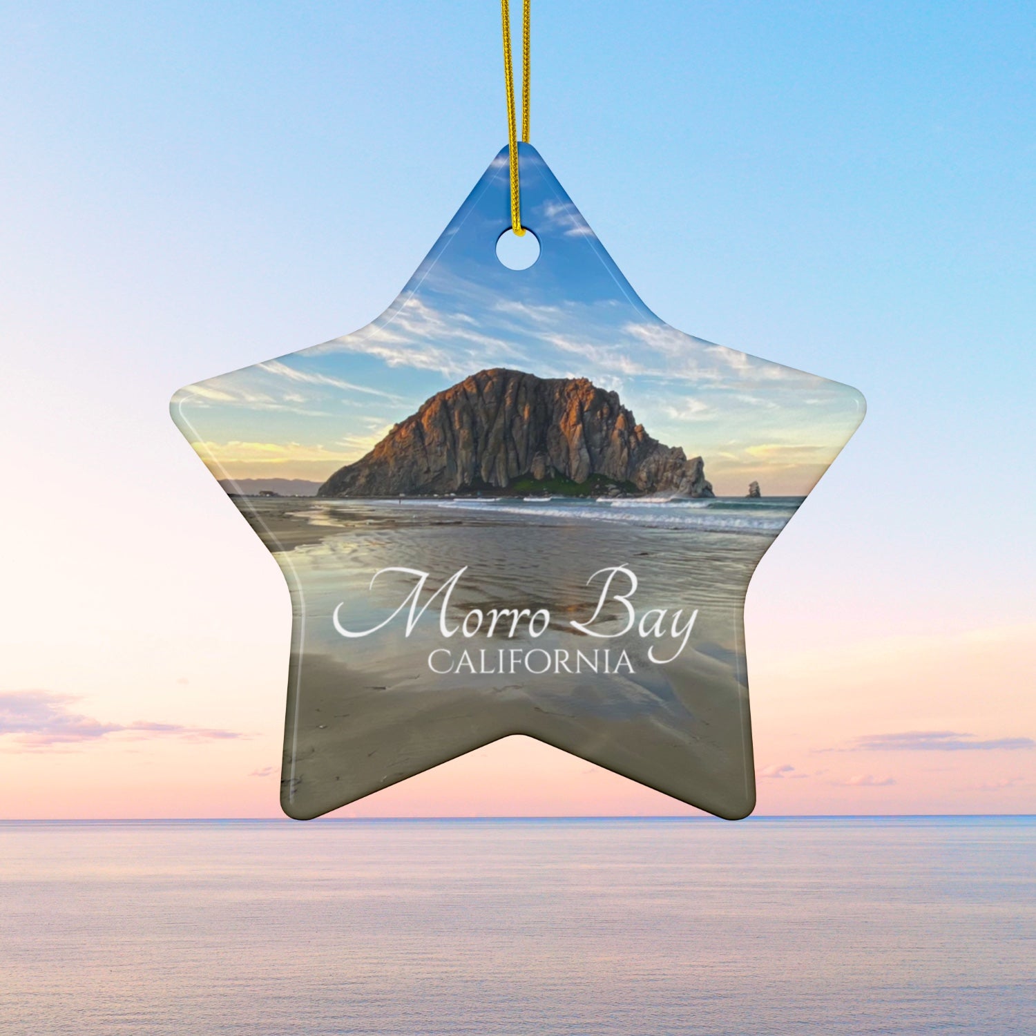 Star-shaped ceramic holiday ornament featuring a photograph of Morro Rock in Morro Bay, California, with reflections in the sand under a dramatic afternoon sky.