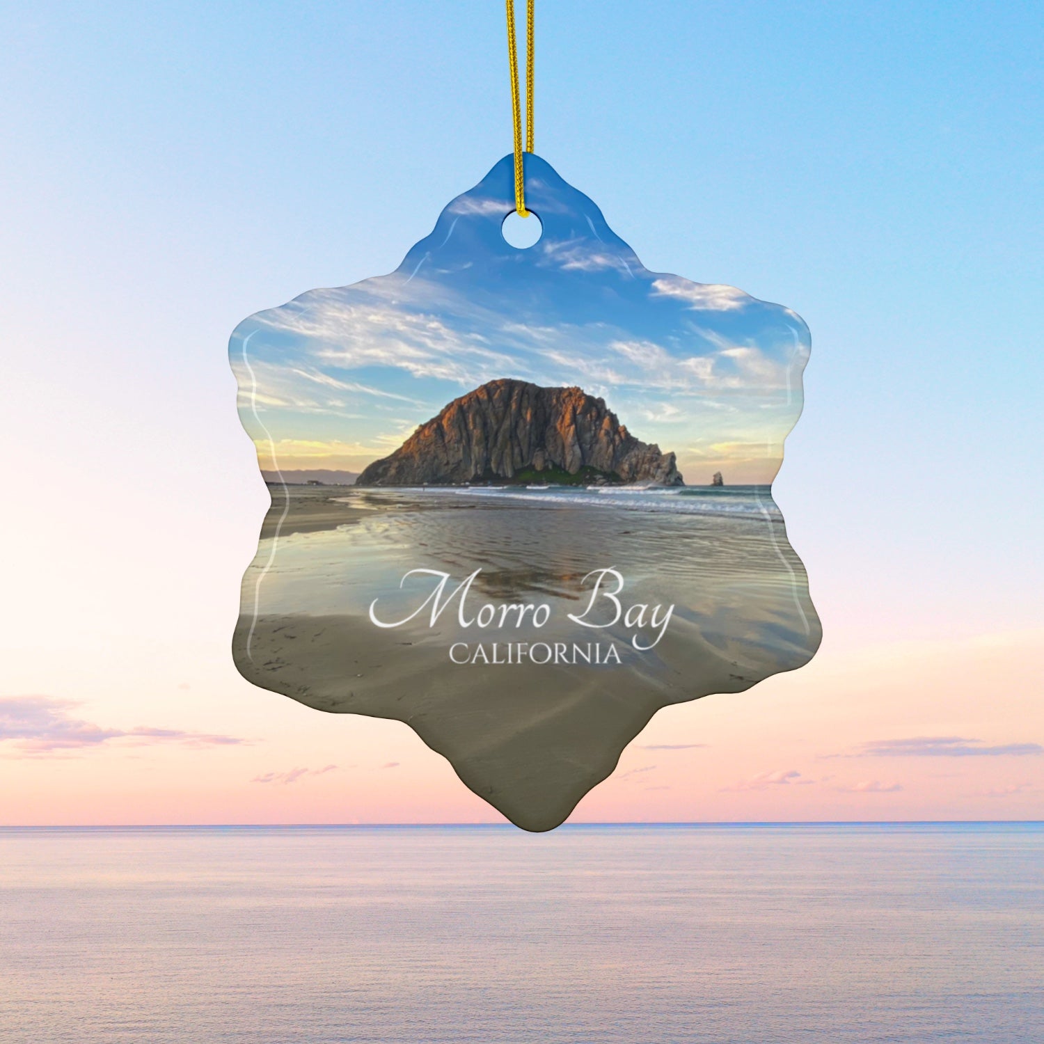 Ceramic holiday ornament featuring a photograph of Morro Rock in Morro Bay, California, with reflections in the sand under a dramatic afternoon sky.