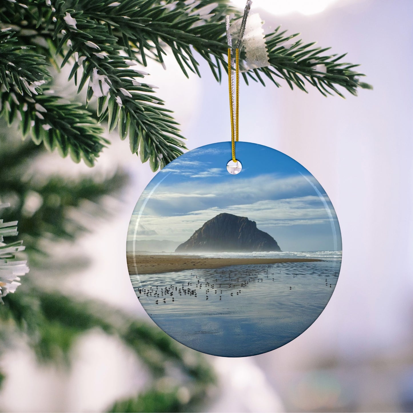 Ceramic holiday ornament featuring a professional photograph of Morro Rock in Morro Bay, California, with the Pacific surf in the foreground,  hanging on a Christmas tree branch.