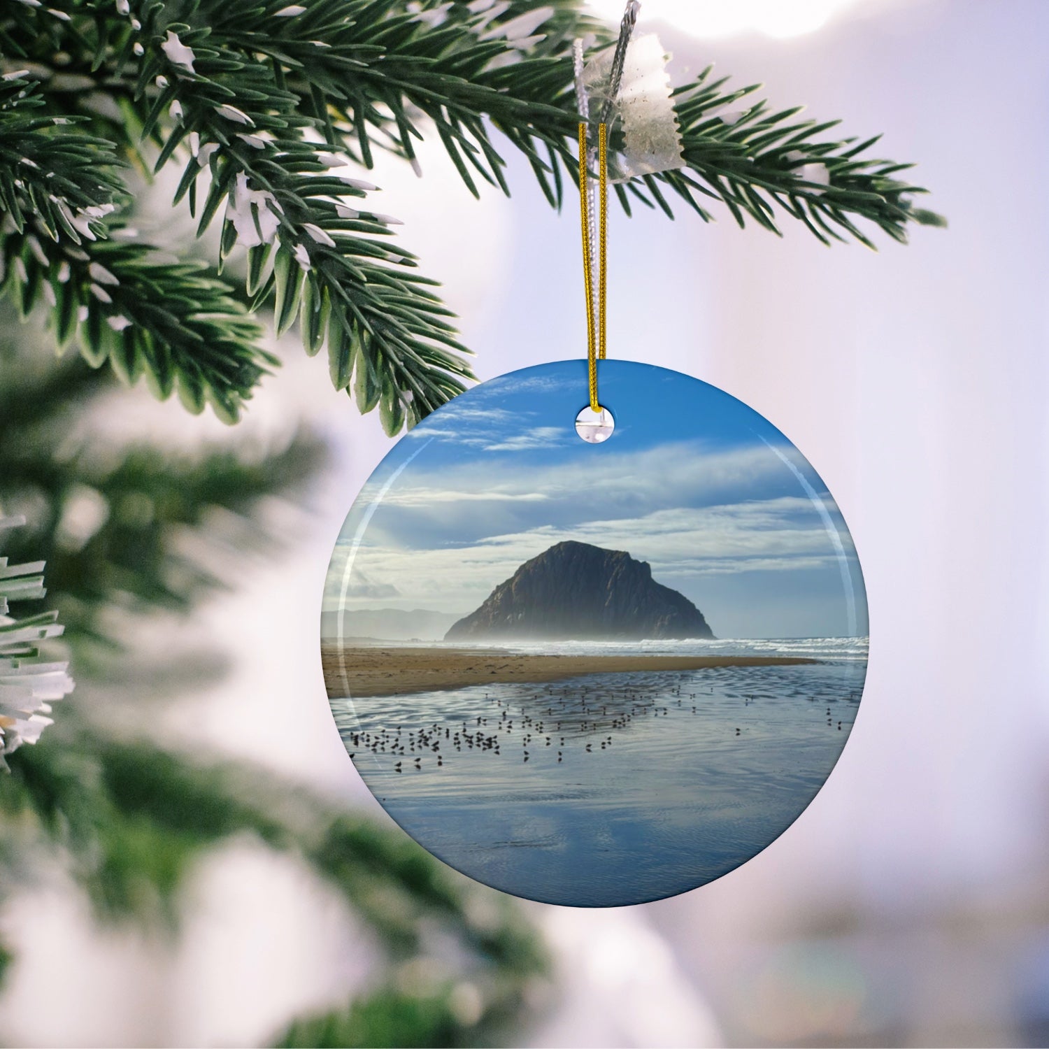 Ceramic holiday ornament featuring a professional photograph of Morro Rock in Morro Bay, California, with the Pacific surf in the foreground,  hanging on a Christmas tree branch.