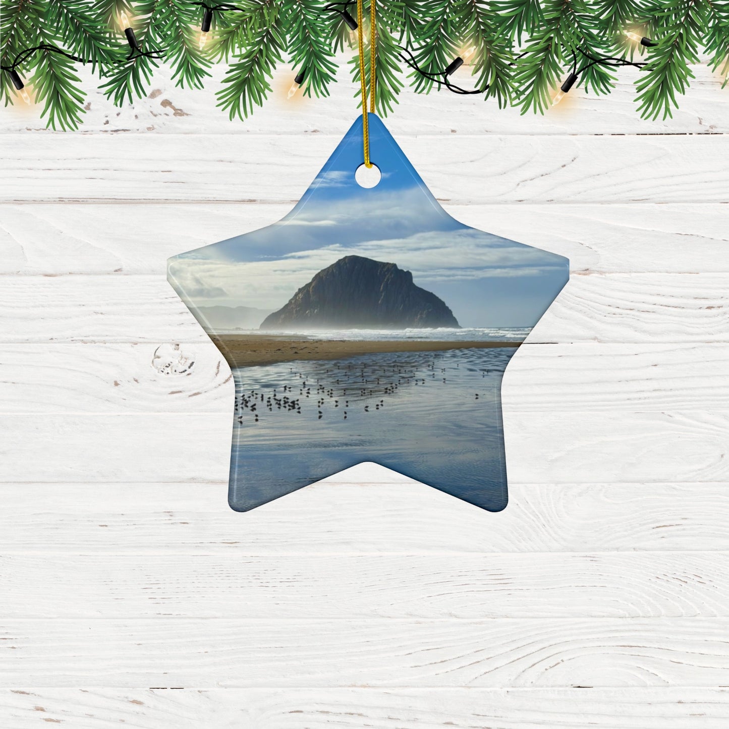 Star-shaped ceramic holiday ornament featuring a professional photograph of Morro Rock in Morro Bay, California, with the Pacific surf in the foreground, hanging on a wooden surface with greenery.