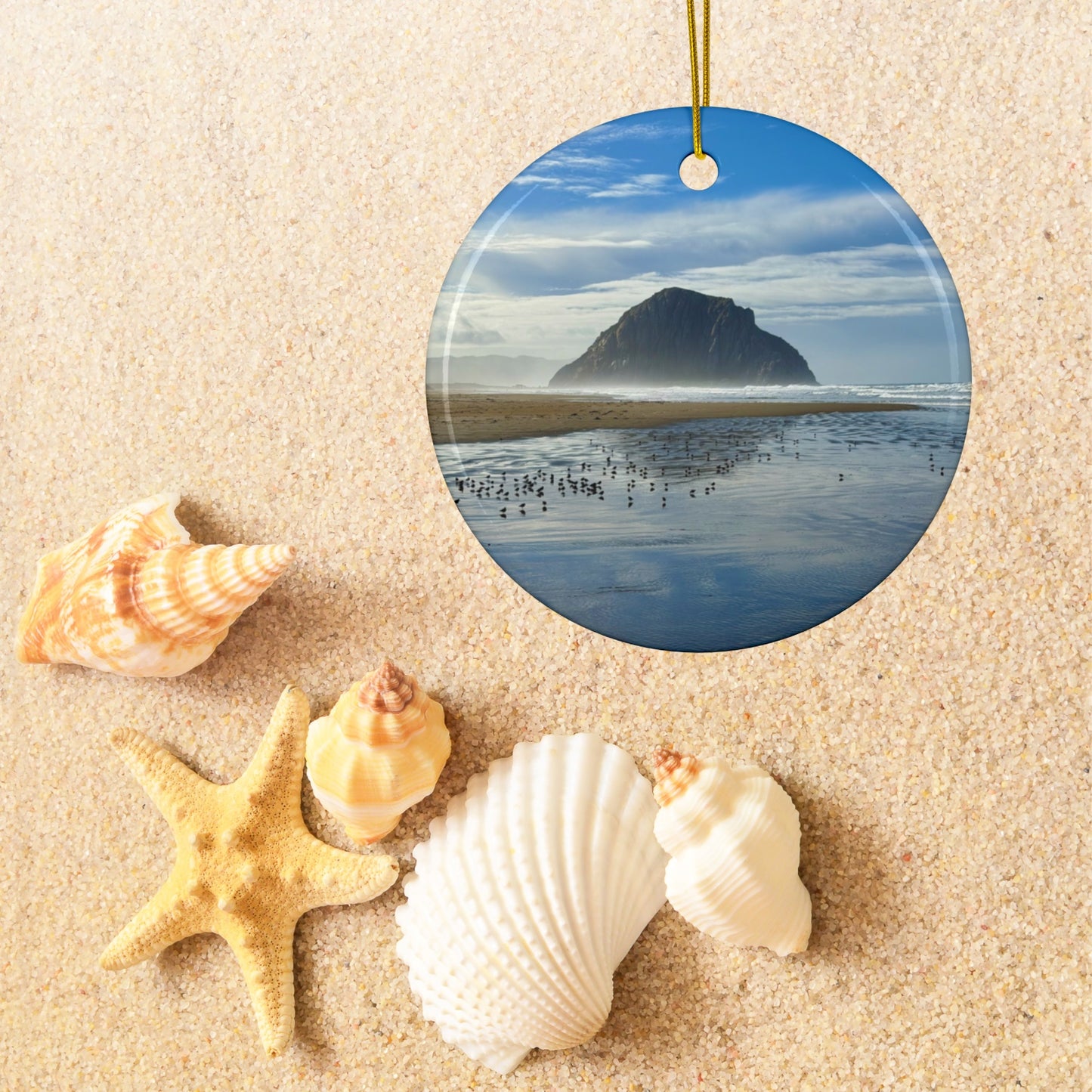 Ceramic holiday ornament featuring a professional photograph of Morro Rock in Morro Bay, California, with the Pacific surf in the foreground, surrounded by seashells on sand.