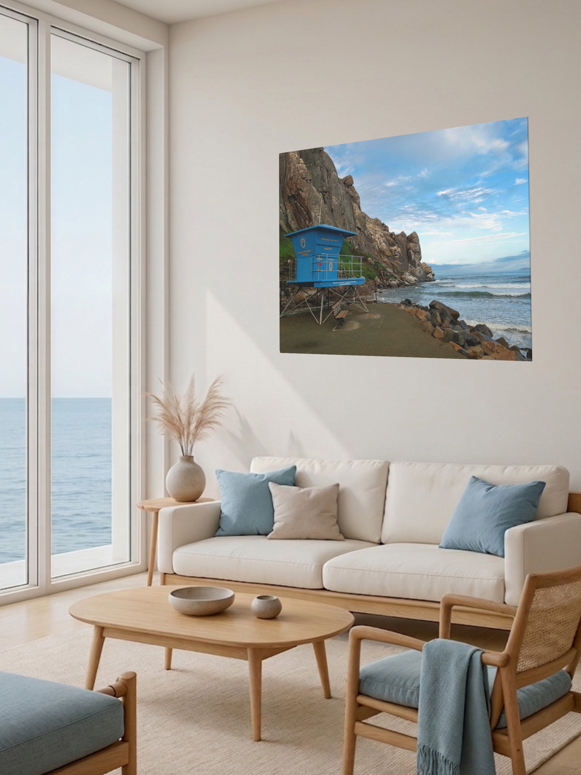 Living room with a large window view of the ocean, a beige sofa with blue pillows, and a blue lifeguard tower at the base of Morro Rock in Morro Bay California canvas print.