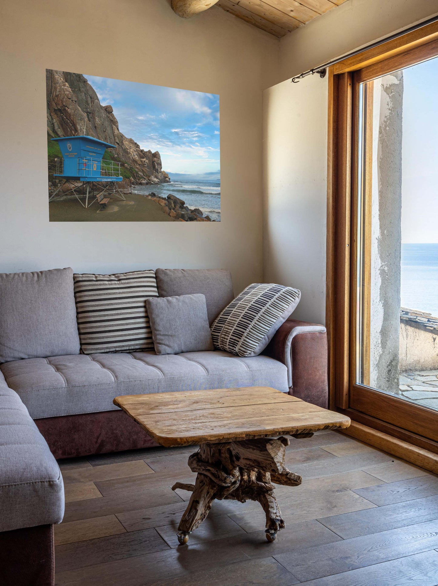 Living room with a gray sofa, wooden coffee table, and a blue lifeguard tower at the base of Morro Rock in Morro Bay California canvas print.