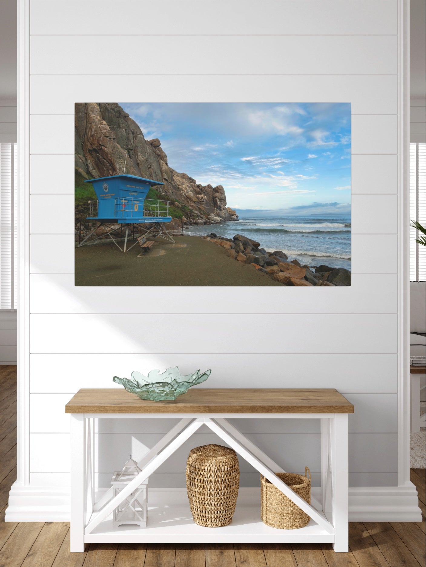Blue lifeguard tower at the base of Morro Rock in Morro Bay California canvas print on a wall above a wooden console table with decorative items.