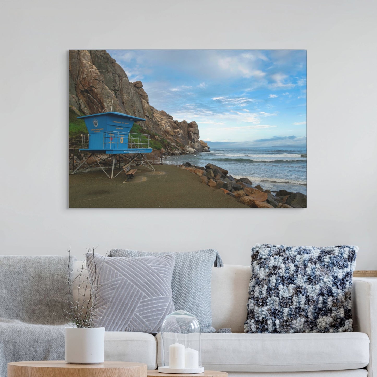 Blue lifeguard tower at the base of Morro Rock in Morro Bay California canvas print on a wall above a sofa with decorative pillows.