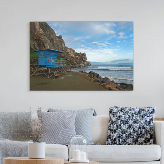 Blue lifeguard tower at the base of Morro Rock in Morro Bay California canvas print on a wall above a sofa with decorative pillows.