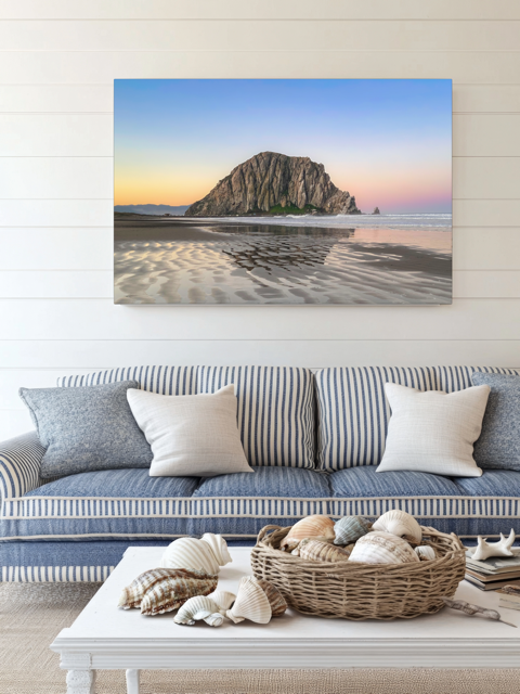 Living room with a couch, coffee table, and a canvas print featuring a Morro Rock morning reflection in wet beach sand.