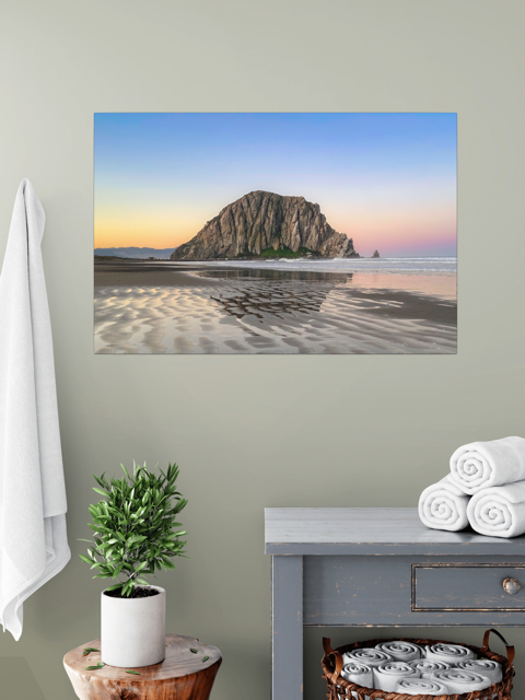 Canvas print featuring a Morro Rock morning reflection in wet beach sand on a wall above a plant and towels.