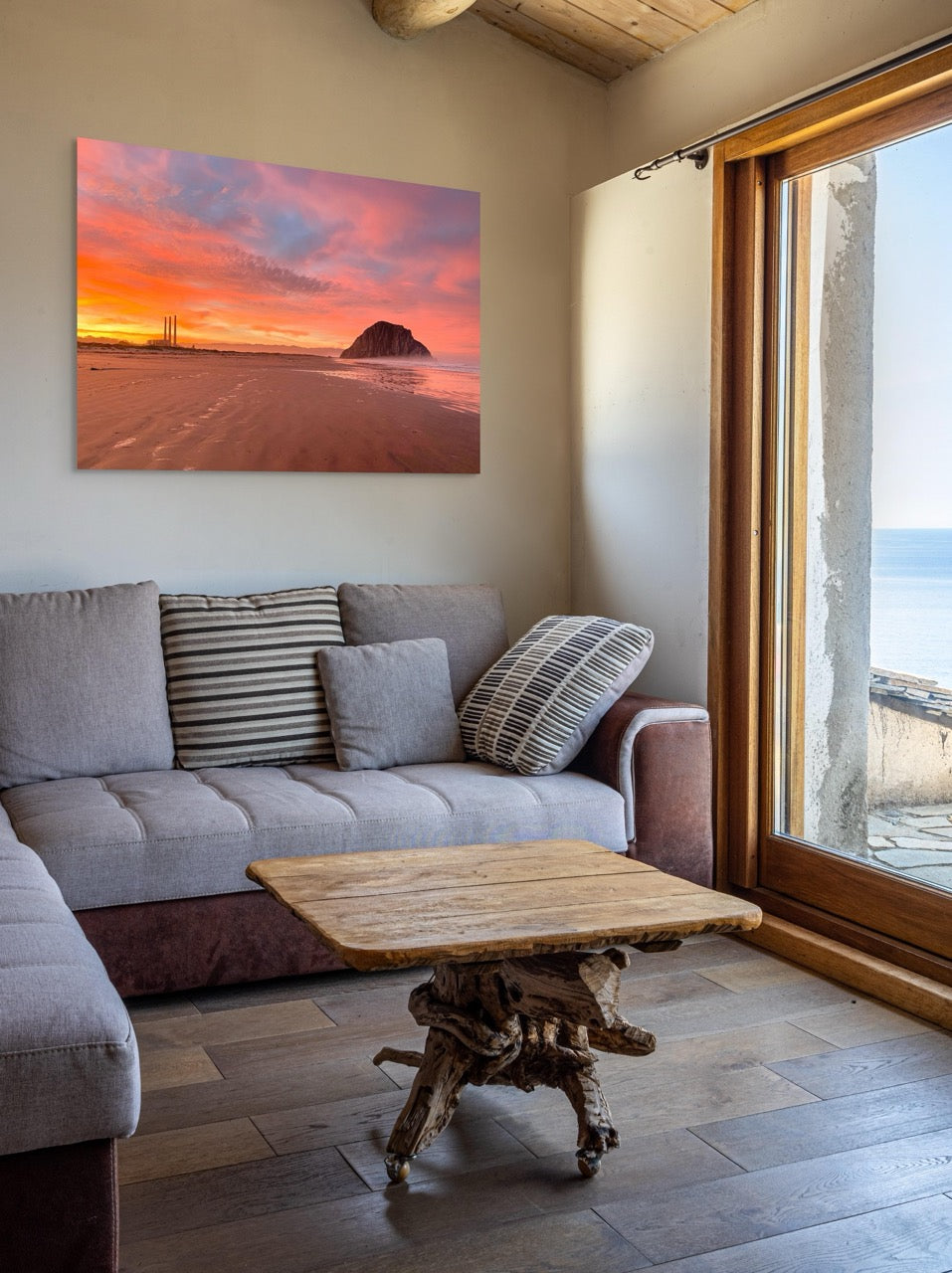 Living room with a gray sofa, wooden coffee table, and a large canvas print of Morro Rock and the stacks at sunrise.