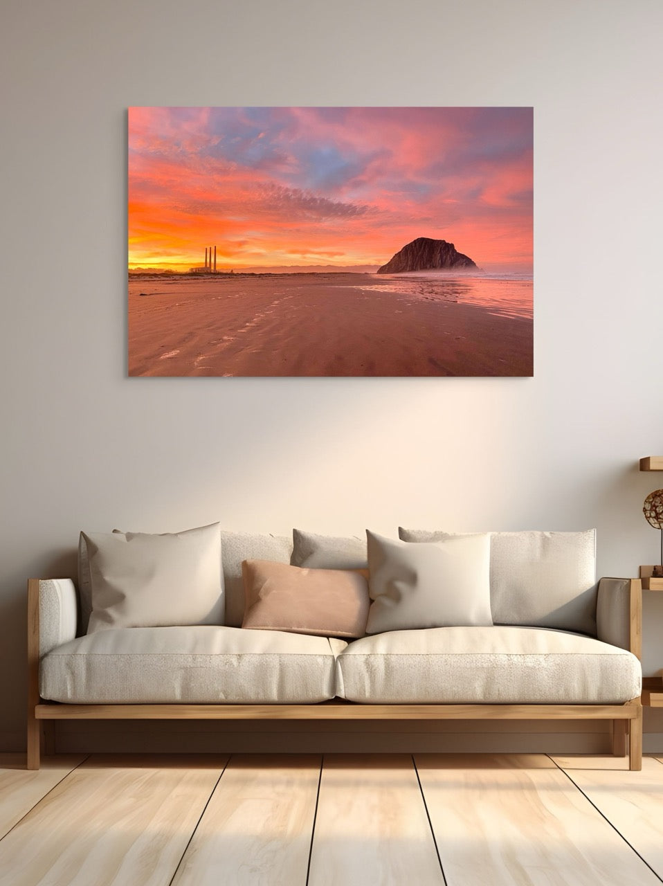 A large canvas print of Morro Rock and the stacks at sunrise above a sofa with cushions