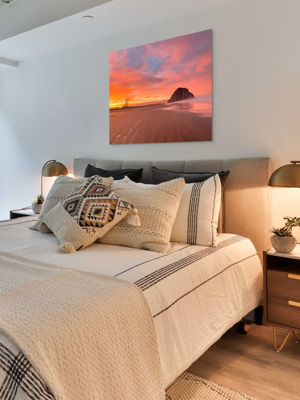 Bedroom with a bed featuring patterned pillows anda canvas print of Morro Rock and the stacks at sunrise on the wall.