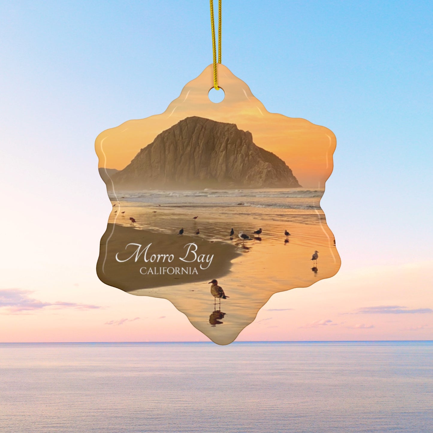 Ceramic Christmas ornament featuring a photograph of a golden sunrise over Morro Rock with shorebirds reflected in the wet sand of the shoreline.