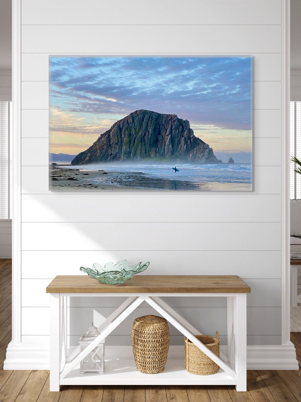 Canvas print of a sunrise at Morro Rock in Morro Bay, California with a surfer on the beach above a wooden bench with storage baskets.
