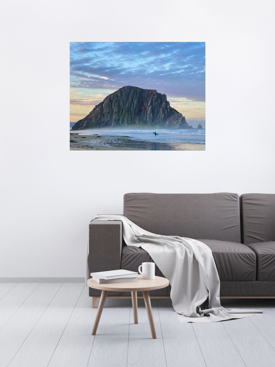 Canvas print of a sunrise at Morro Rock in Morro Bay, California with a surfer on the beach in a living room with a gray sofa, small round table.