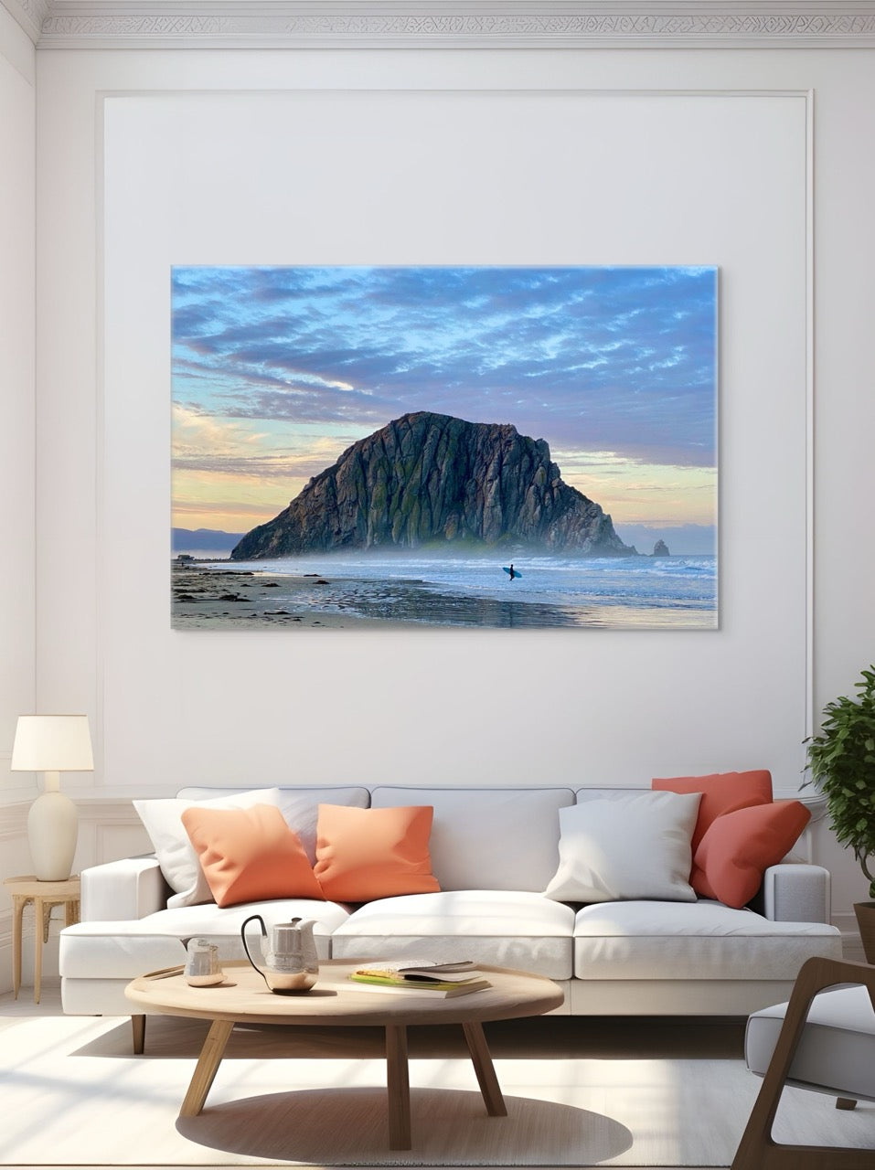 Canvas print of a sunrise at Morro Rock in Morro Bay, California with a surfer on the beach on the wall above a white sofa.