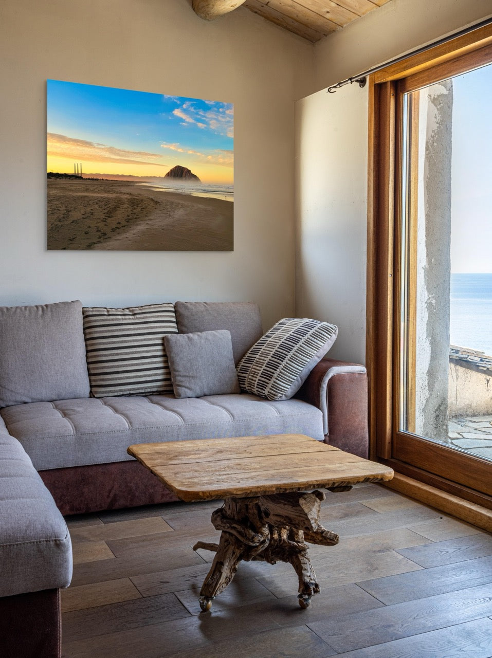 Living room with a gray sofa, wooden coffee table, and a large canvas print of Morro Rock and the stack at sunrise.