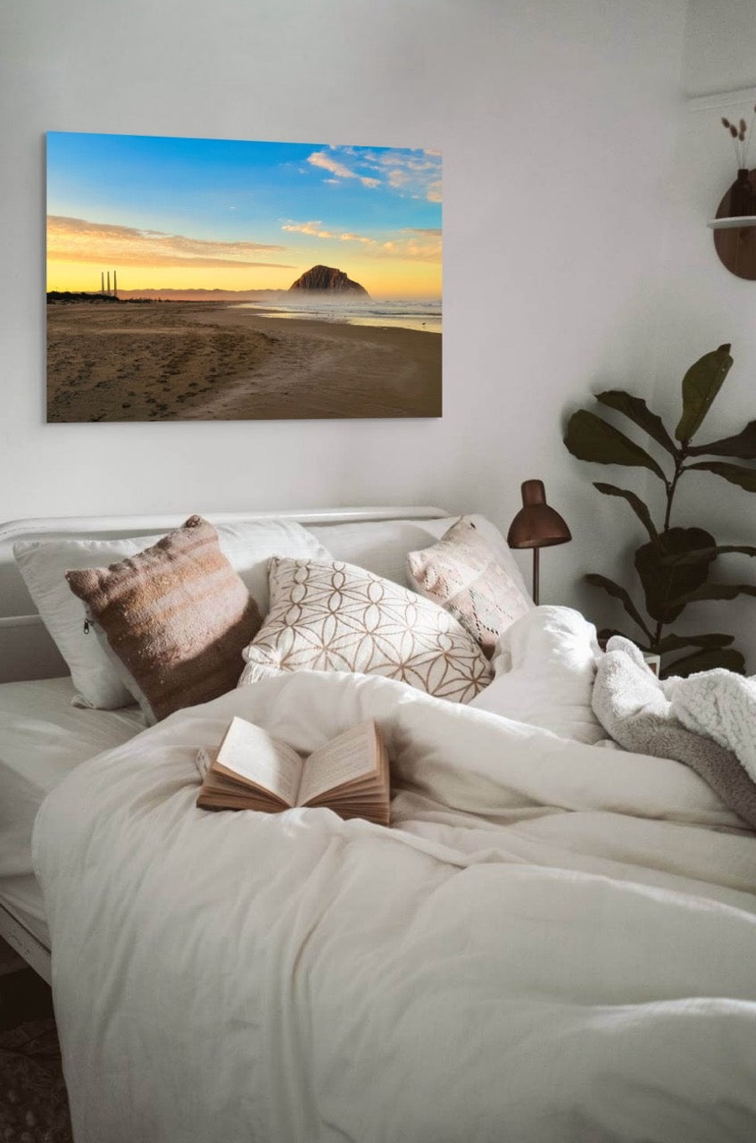 Bedroom with a large bed, decorative pillows, and a canvas print of Morro Rock and the stack at sunrise.
