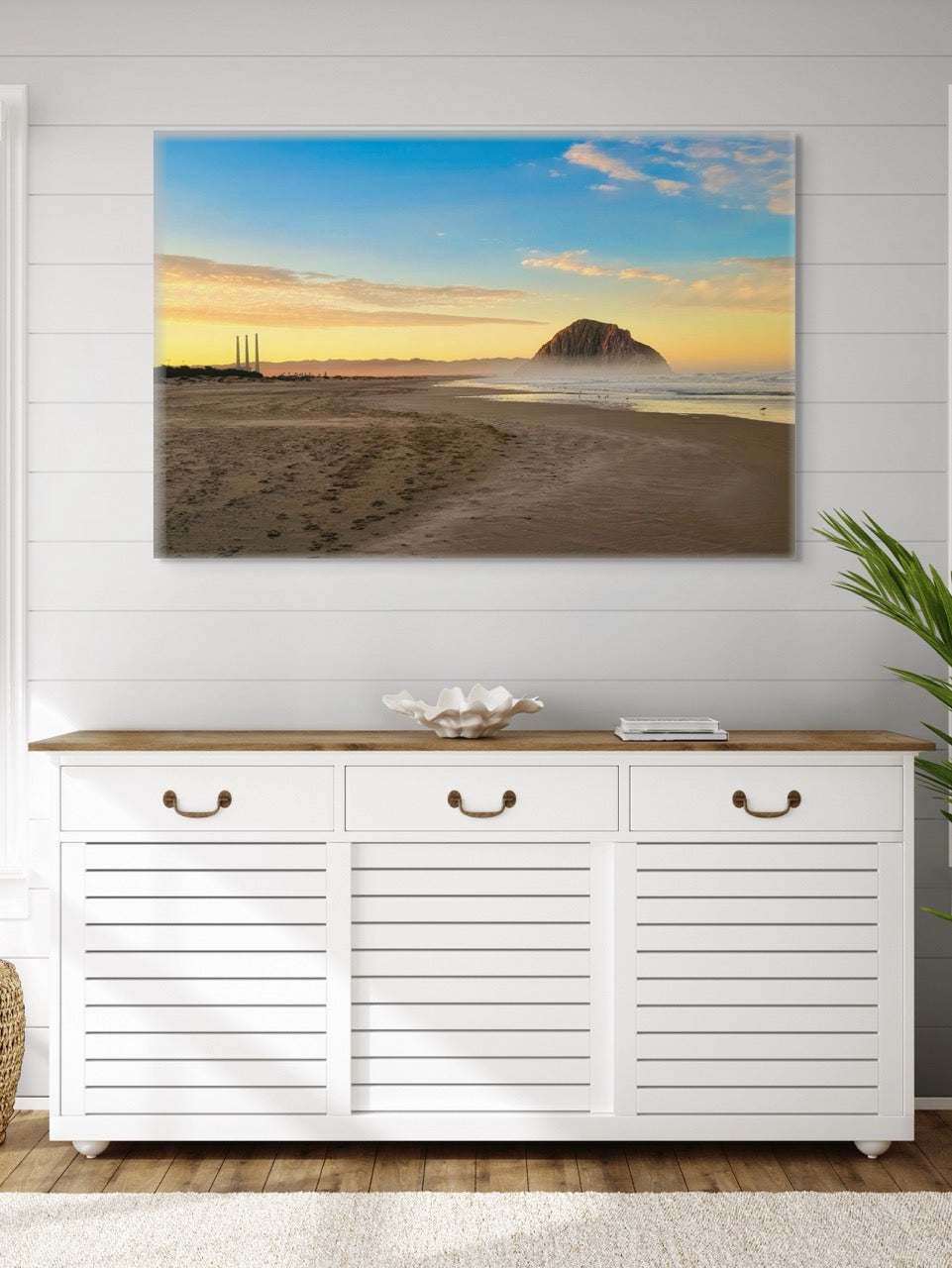 White cabinet with wooden top below a canvas print of Morro Rock and the stack at sunrise on a white wall.
