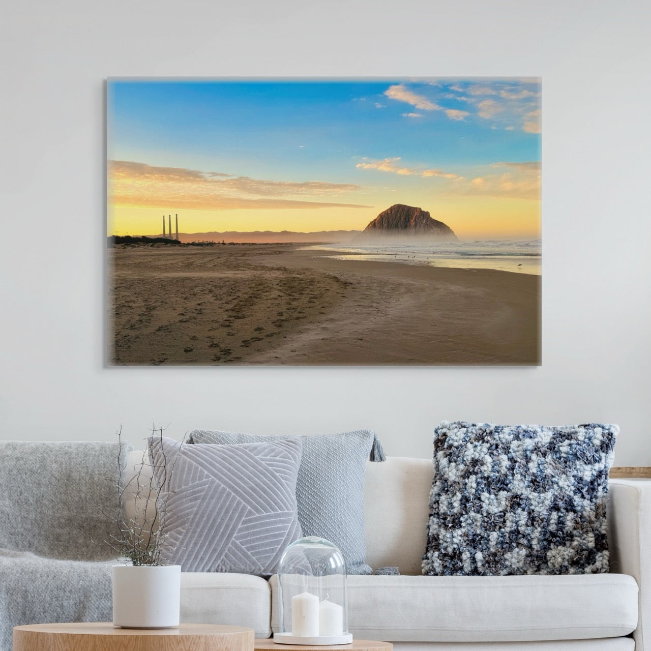 Morro Rock and stacks at sunrise canvas print on a wall above a sofa with decorative pillows.