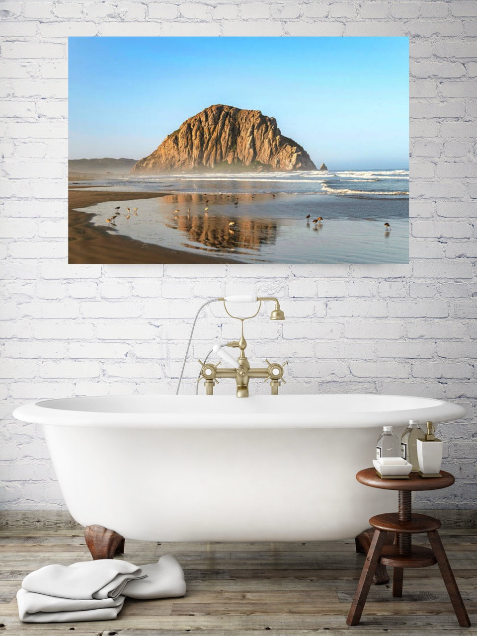 Bathroom with a freestanding bathtub, wooden stool, and canvas print of Morro Rock reflecting in the wet sand with birds on the shoreline.