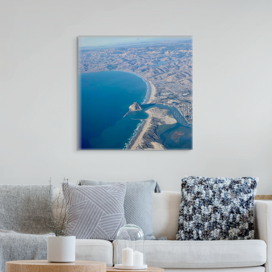 Aerial photography of Morro Rock and California coastline canvas print on a wall above a living room with a sofa and decorative pillows.