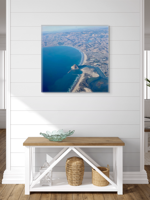 Aerial photography of Morro Rock and California coastline canvas print on a white wall above a wooden console table.