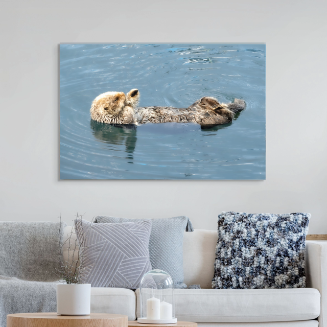 Canvas print of a sea otter in water hanging on a wall above a living room sofa.