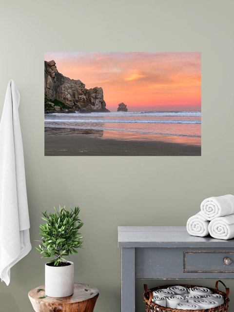 Beach scene with sunset on a wall above a table with a plant and folded towels.